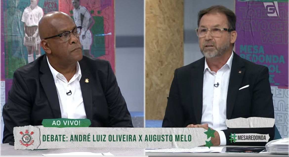 André Luiz à esquerda e Augusto Melo à direita, ambos de terno, em debate.